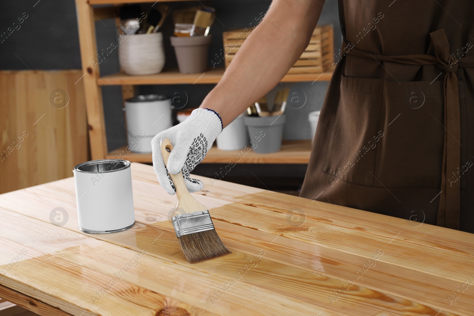 Photo of Man varnishing wooden surface with brush indoors, closeup