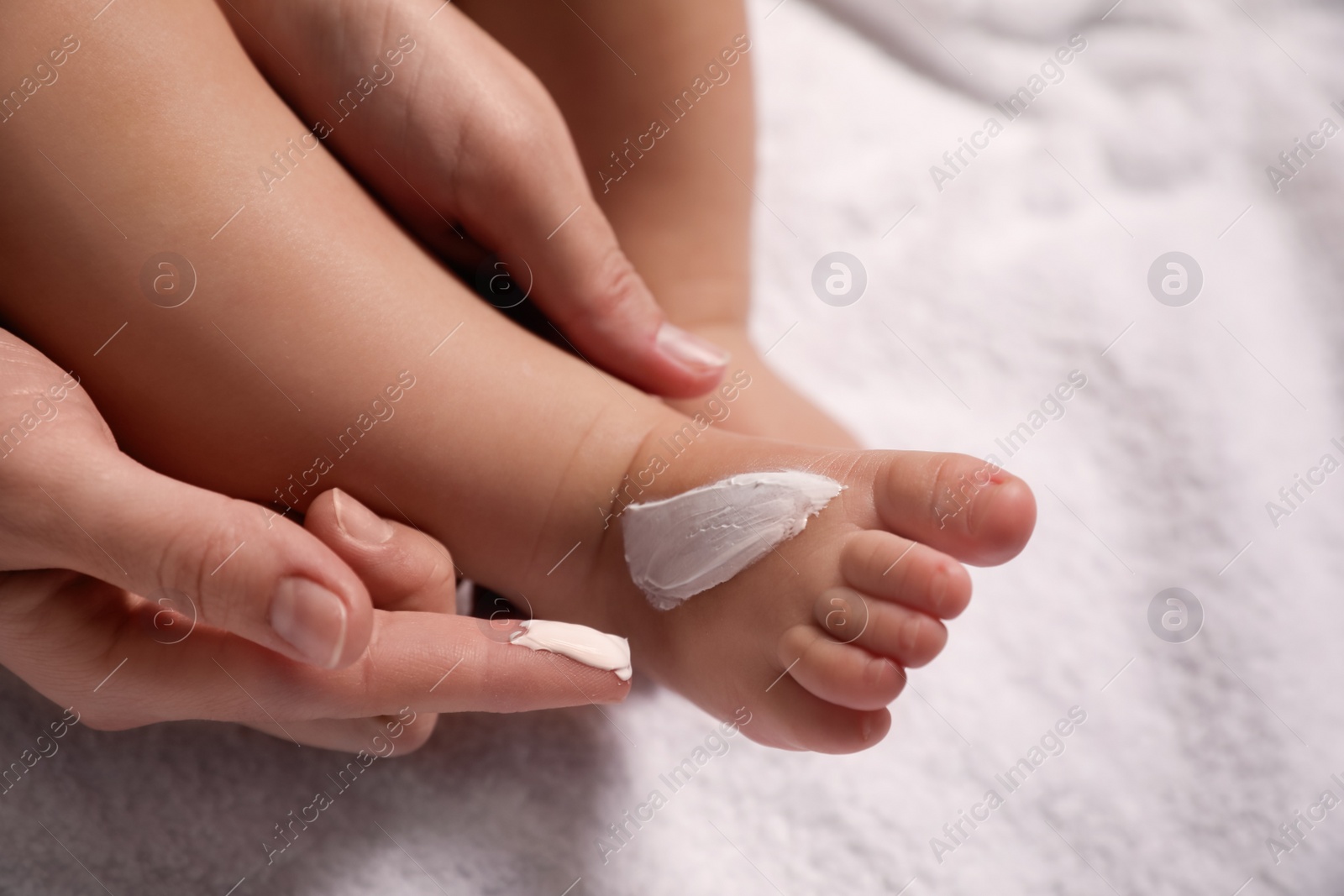 Photo of Mother applying moisturizing cream onto her little baby's skin on white towel, closeup