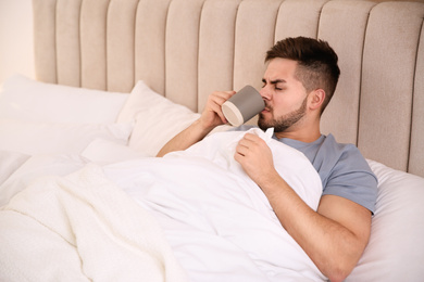 Photo of Sick young man with cup of hot drink in bed at home. Influenza virus