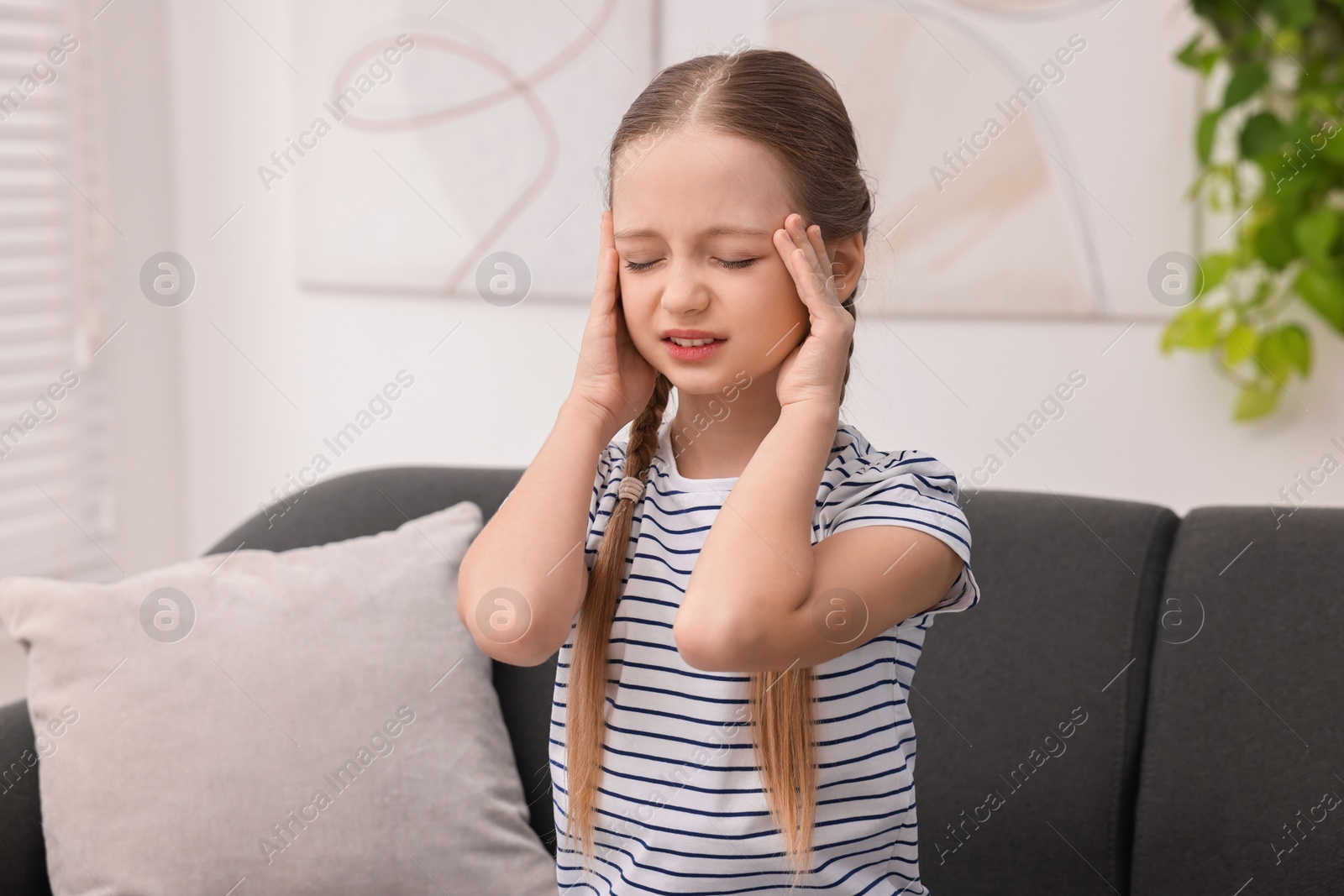 Photo of Little girl suffering from headache on sofa indoors