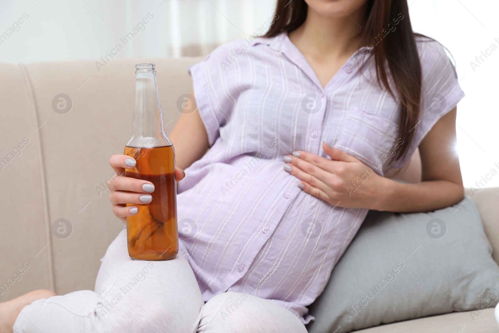 Photo of Future mother with bottle of beer at home, closeup. Alcohol abuse during pregnancy