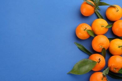 Fresh tangerines with green leaves on blue background, flat lay. Space for text