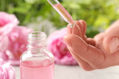 Photo of Woman dripping rose essential oil on finger near bottle, closeup
