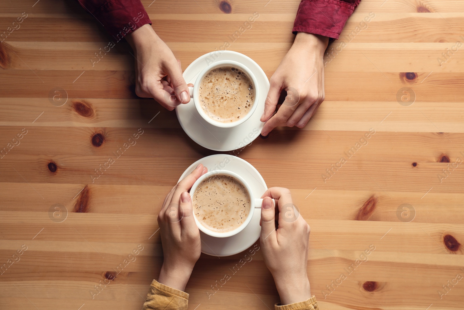 Photo of Women with cups of coffee at wooden table, top view