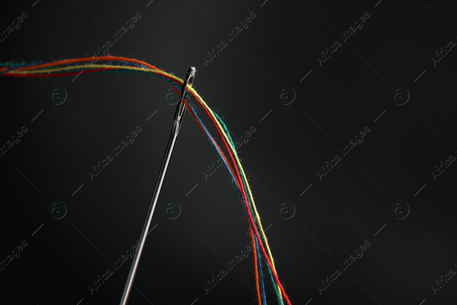 Photo of Sewing needle with colorful threads on black background, space for text