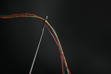 Sewing needle with colorful threads on black background, space for text