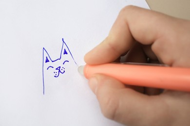 Photo of Child erasing drawing with erasable pen on paper sheet against beige background, closeup