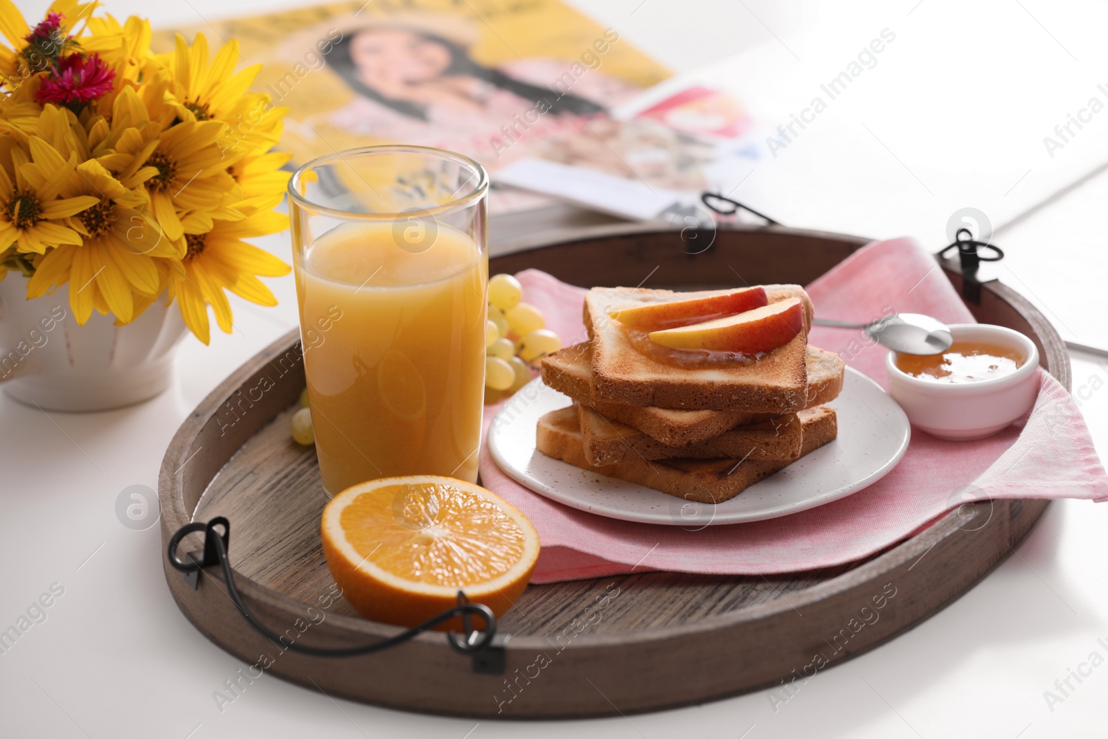 Photo of Wooden tray with delicious breakfast and beautiful flowers on white table