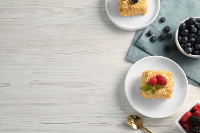 Pieces of Napoleon cake, berries and spoon on wooden table, flat lay with space for text