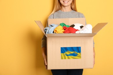 Image of Humanitarian aid for Ukrainian refugees. Woman holding box with donations on color background. Space for text