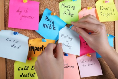 Woman pinning paper note with phrase Meeting On Friday to cork board, closeup