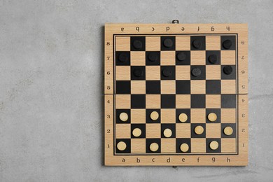 Photo of Wooden checkerboard with game pieces on light grey background, top view. Space for text