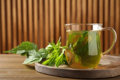 Glass cup of aromatic nettle tea and green leaves on wooden table, space for text