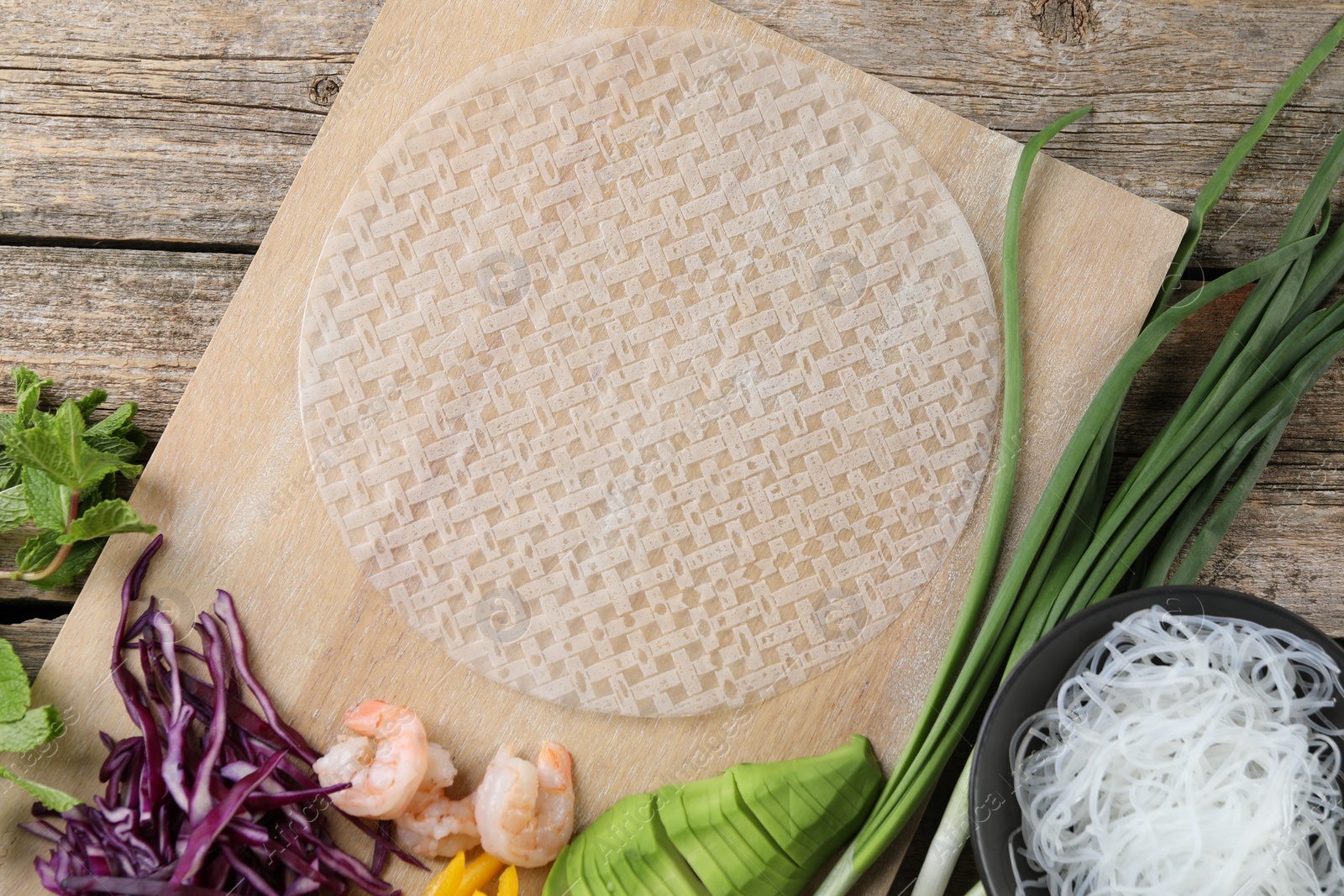 Photo of Rice paper and other ingredients for spring rolls on wooden table, top view