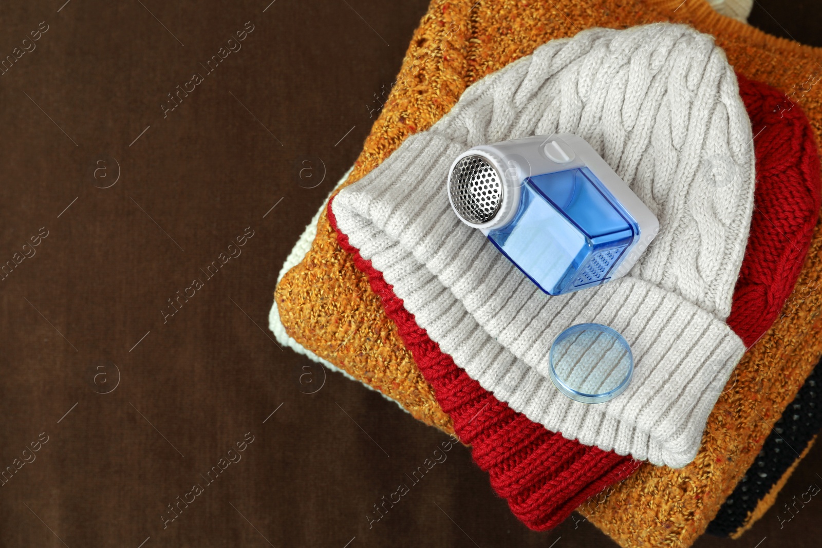 Photo of Fabric shaver and knitted clothes on brown background, top view. Space for text