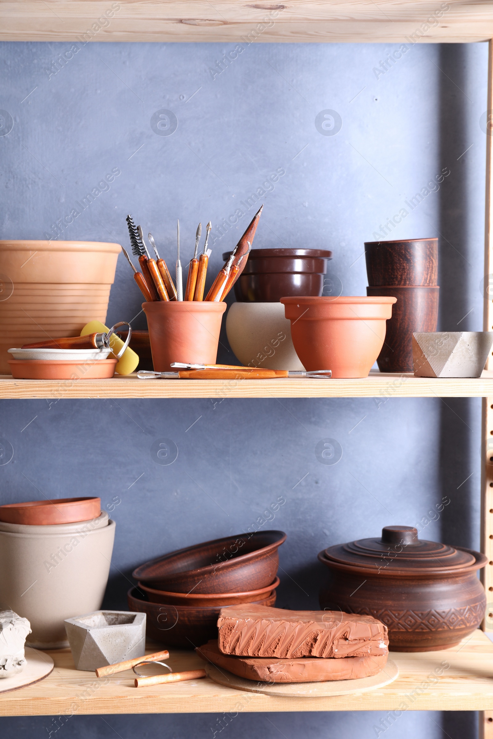 Photo of Set of different crafting tools and clay dishes on wooden rack in workshop