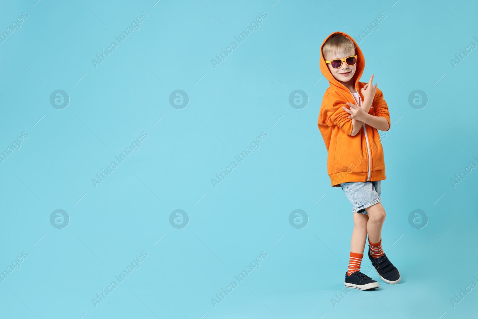 Photo of Happy little boy dancing on light blue background. Space for text