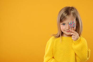 Portrait of cute little girl with lollipop on orange background. Space for text