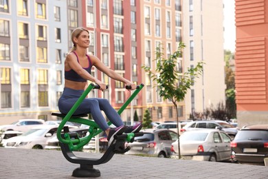 Photo of Happy woman training on rowing machine at outdoor gym, space for text