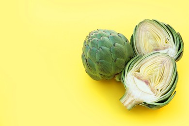 Whole and cut fresh raw artichokes on pale yellow background. Space for text