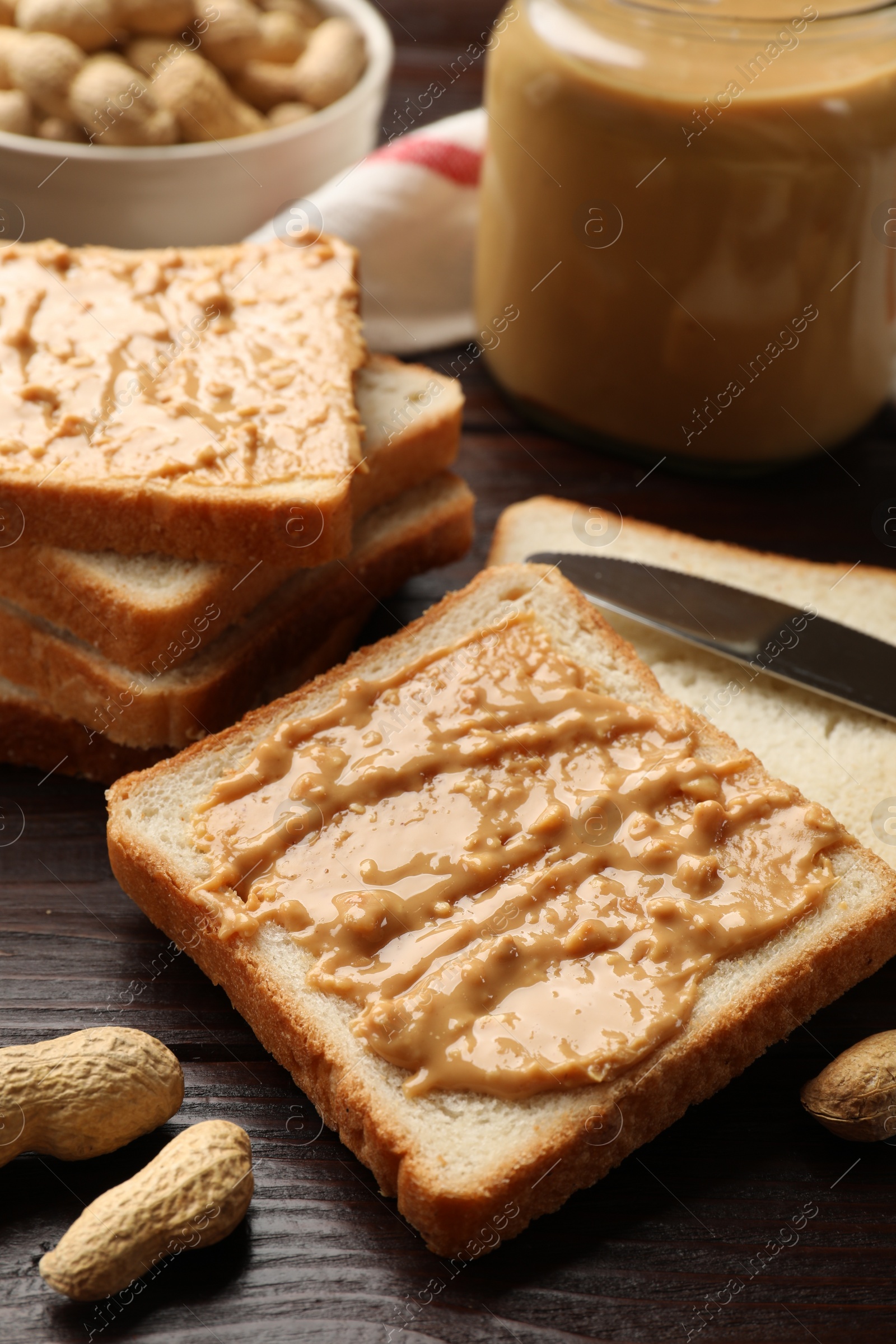 Photo of Delicious toasts with peanut butter, nuts and knife on dark wooden table