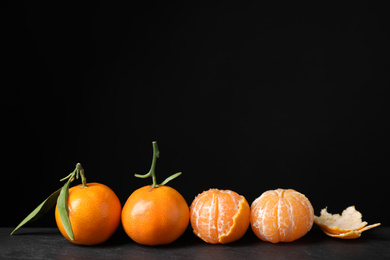 Photo of Fresh ripe tangerines on table against black background. Space for text