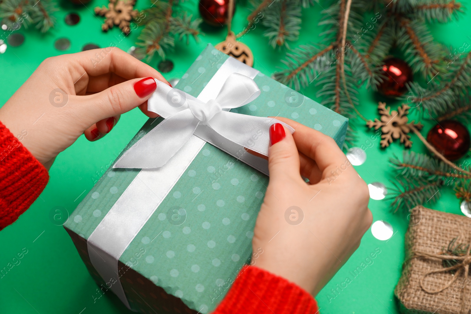 Photo of Woman with gift box near fir tree branches and Christmas decor on green background, closeup