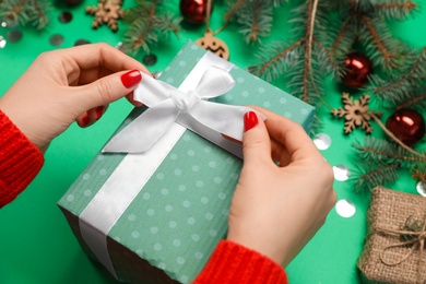 Woman with gift box near fir tree branches and Christmas decor on green background, closeup