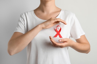 Photo of Woman with red ribbon on t-shirt against light background. Cancer awareness