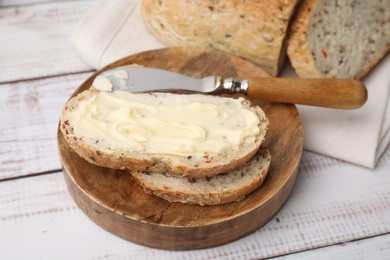 Tasty bread with butter and knife on white wooden table, closeup