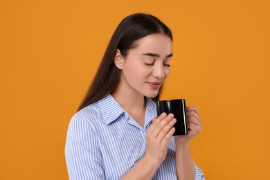 Photo of Beautiful young woman holding black ceramic mug on orange background