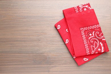 Photo of Folded red bandana with paisley pattern on wooden table, top view. Space for text