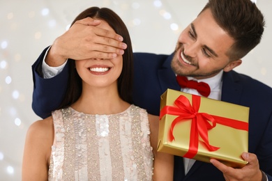 Photo of Young man presenting gift to his girlfriend against blurred festive lights. Christmas celebration