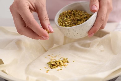 Photo of Woman putting filling into baking dish with dough to prepare baklava, closeup