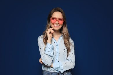 Portrait of beautiful young woman with heart shaped sunglasses on color background