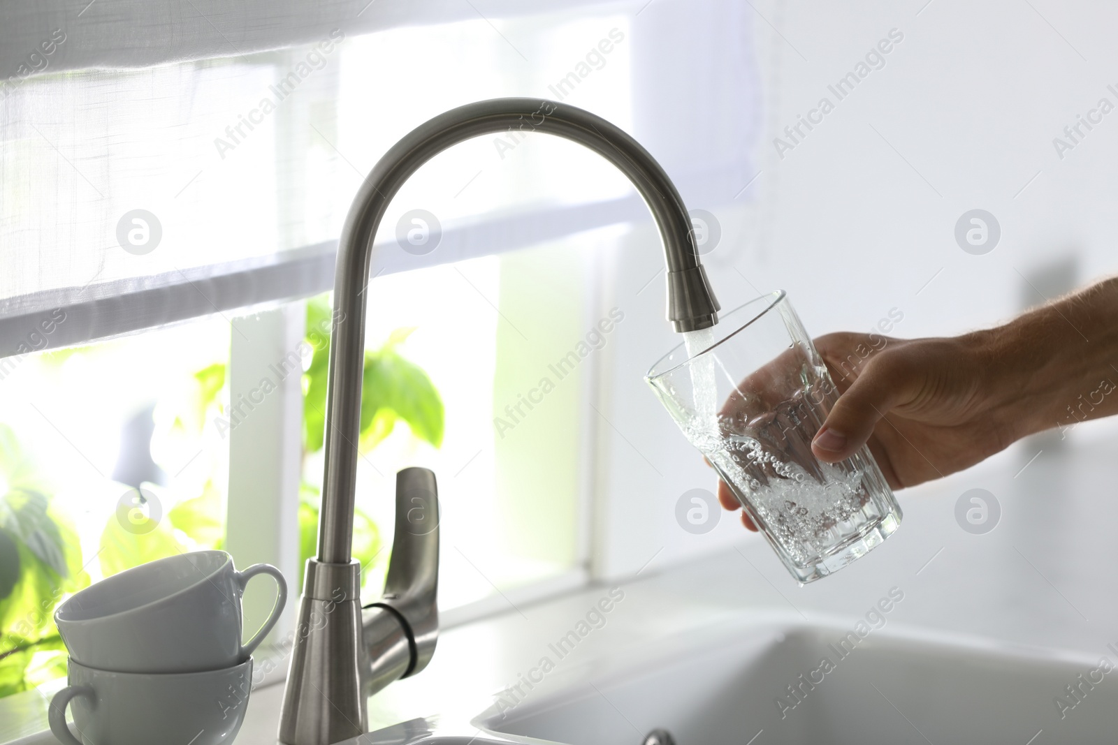 Photo of Man pouring water into glass in kitchen, closeup