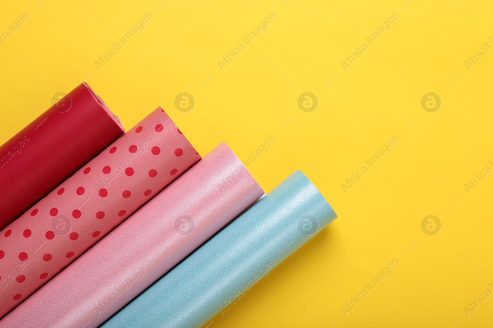 Photo of Rolls of colorful wrapping papers on yellow background, flat lay. Space for text