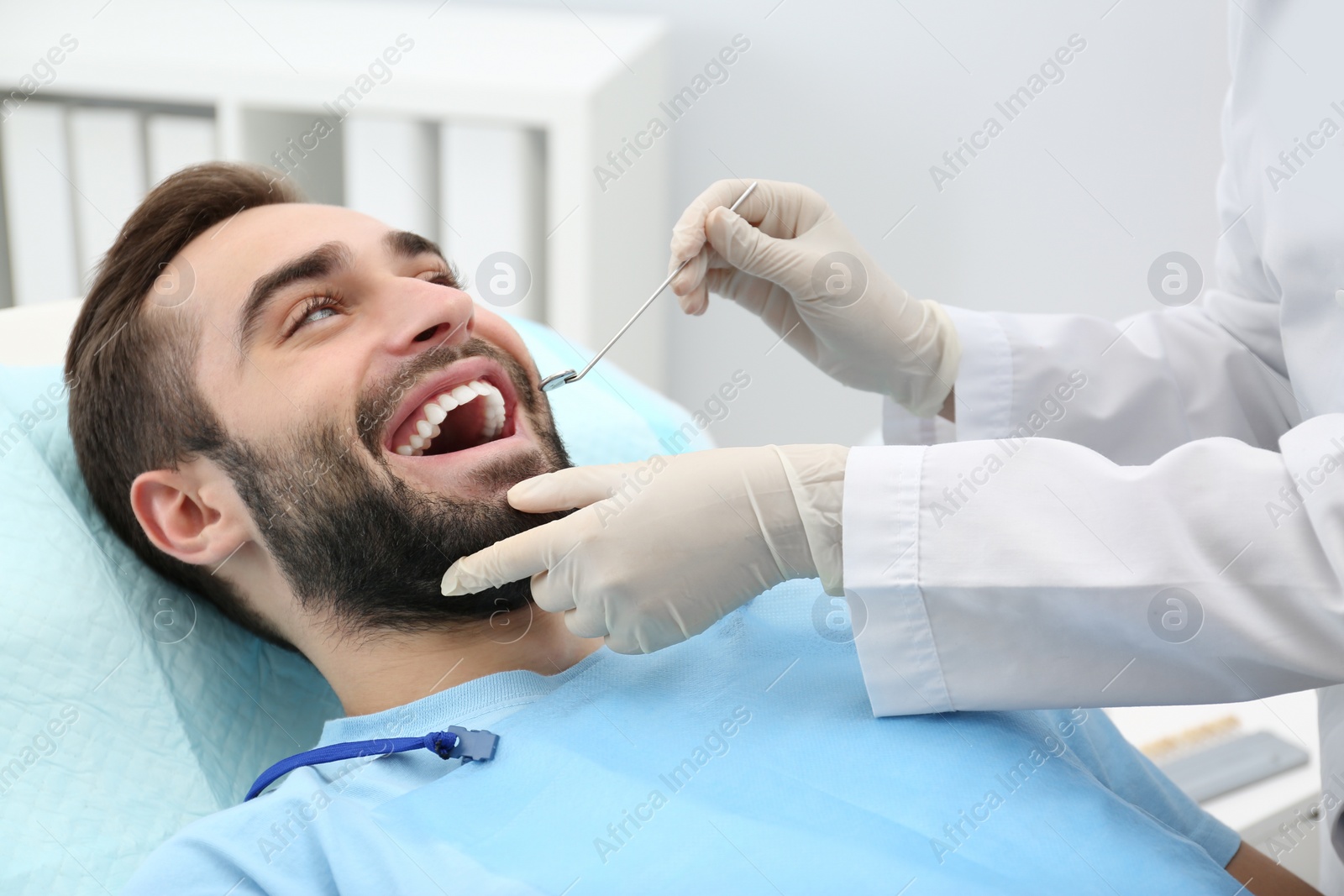 Photo of Dentist examining young man's teeth with mirror in hospital