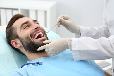 Dentist examining young man's teeth with mirror in hospital