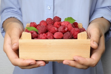 Photo of Woman holding small wooden crate with delicious ripe raspberries, closeup