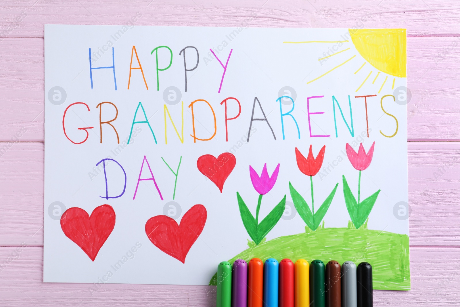 Photo of Beautiful drawing with phrase Happy Grandparents Day on pink wooden table, flat lay