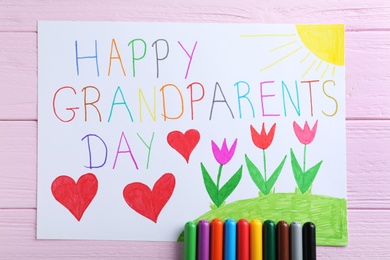 Photo of Beautiful drawing with phrase Happy Grandparents Day on pink wooden table, flat lay