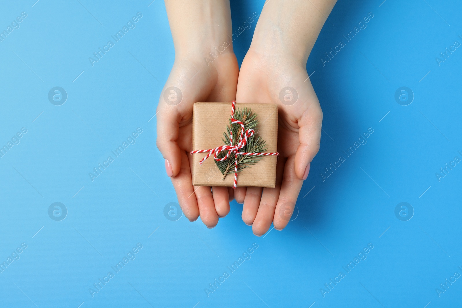 Photo of Christmas present. Woman holding beautifully wrapped gift box on light blue background, top view