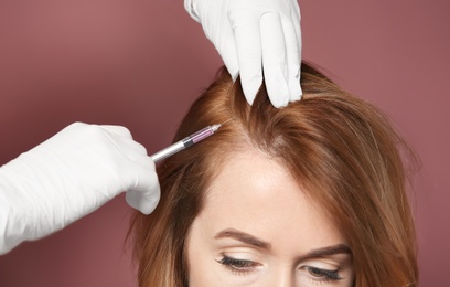 Young woman with hair loss problem receiving injection, on color background