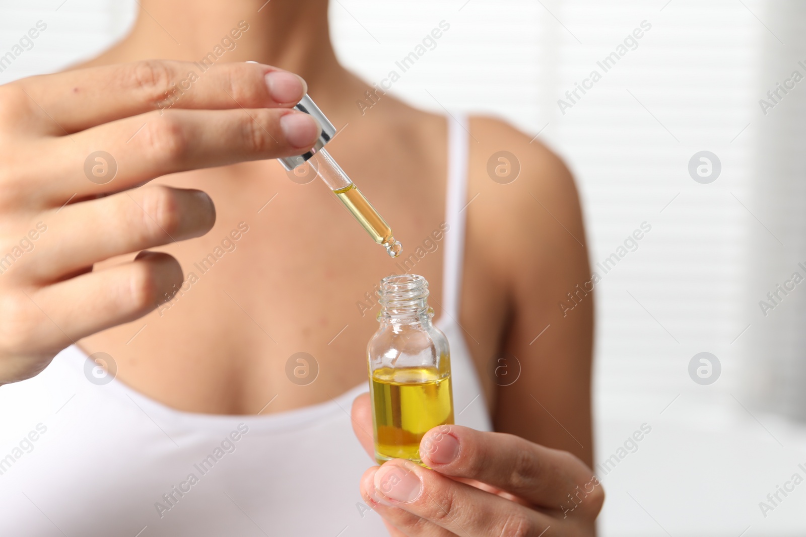 Photo of Woman with bottle of cosmetic serum on light background, closeup