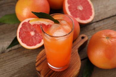 Photo of Tasty grapefruit drink with ice in glass and fresh fruits on wooden table, closeup