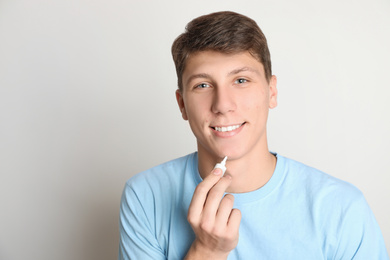 Photo of Teen guy with acne problem applying cream on light background