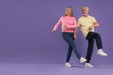 Senior couple dancing together on purple background, space for text