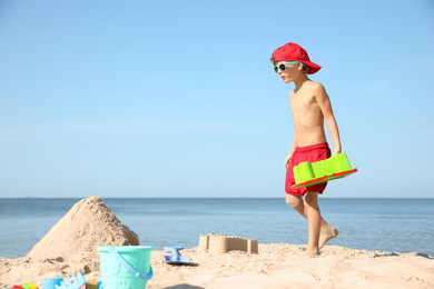 Photo of Cute little child playing with plastic toys at sandy beach on sunny day
