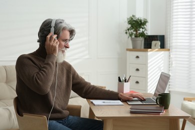 Photo of Middle aged man with laptop and headphones learning at table indoors